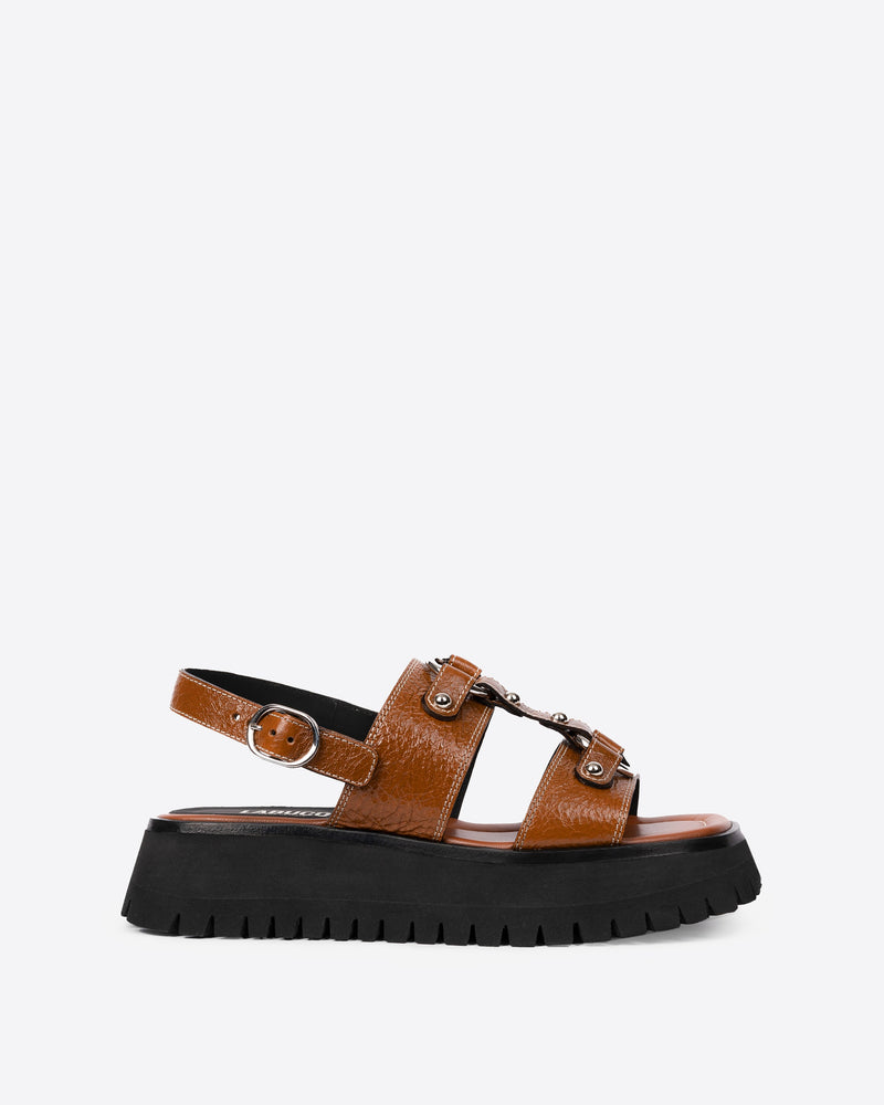 Tan (brown) colored sandal with a buckle, studs, and a treaded outsole on a white background